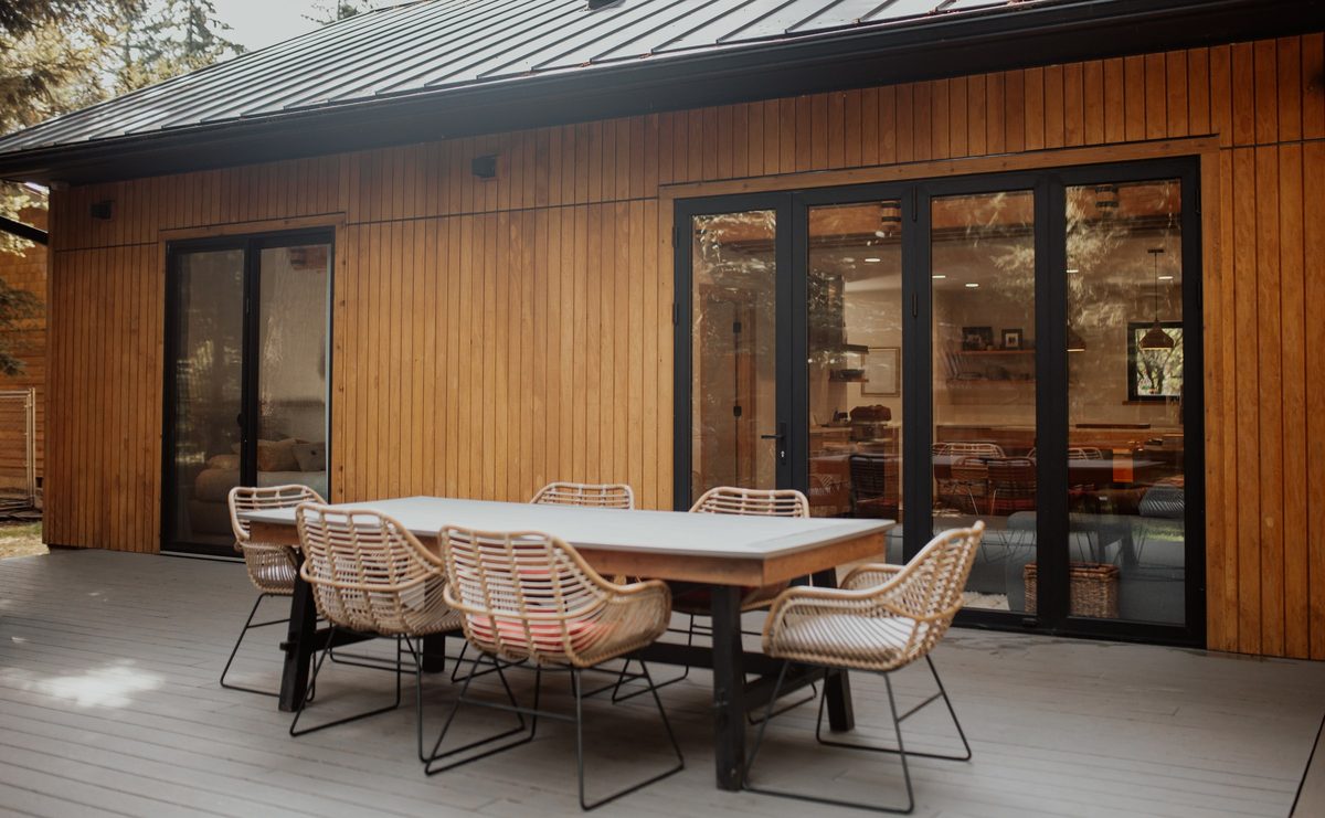 Finished cabin deck with an outdoor dining table, cedar siding, and glazed doors