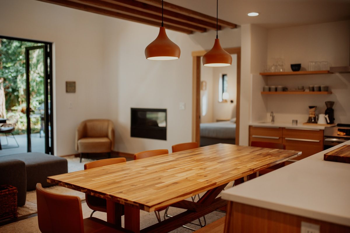 Handmade dining table beside the cabin living area, fireplace, and exposed loft beams