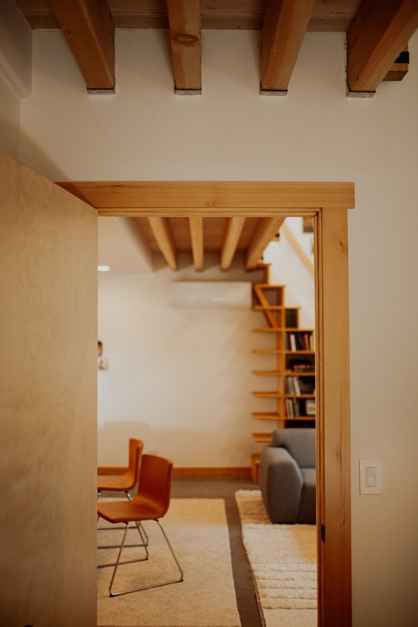View through a wood-trimmed interior doorway toward the living area and bookcase staircase