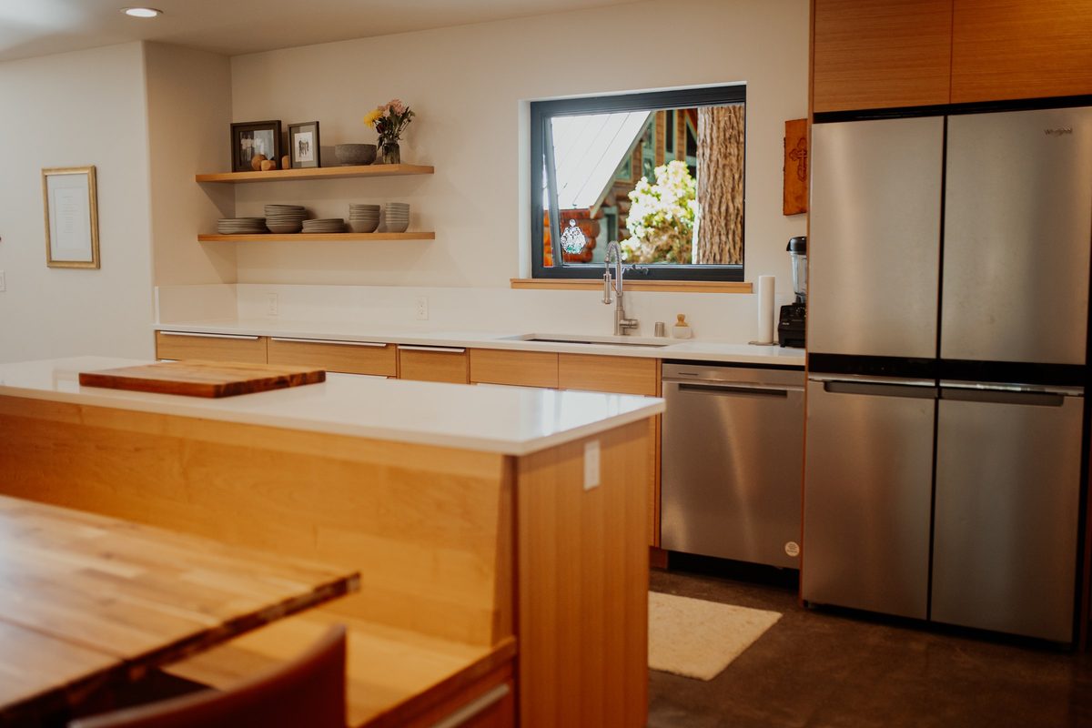 Cabin kitchen with wood cabinetry, a white island, open shelves, and a window above the sink