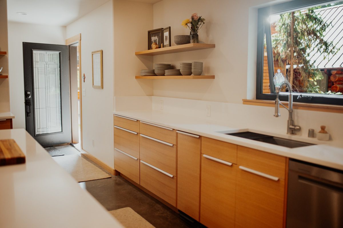 Long kitchen counter with wood drawers, open shelves, and a window above the sink