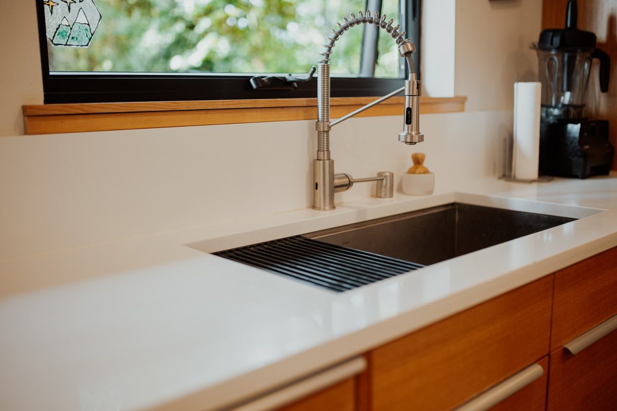 Kitchen sink, faucet, and white worktop beneath the cabin window