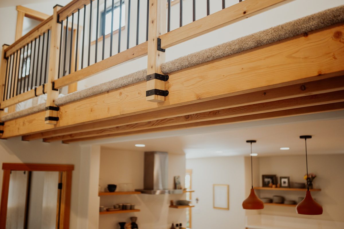 Exposed loft beam connections and wood railing above the cabin kitchen